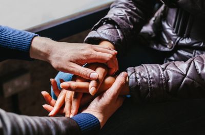 Person with hands folded and another with their hands on top of theirs 